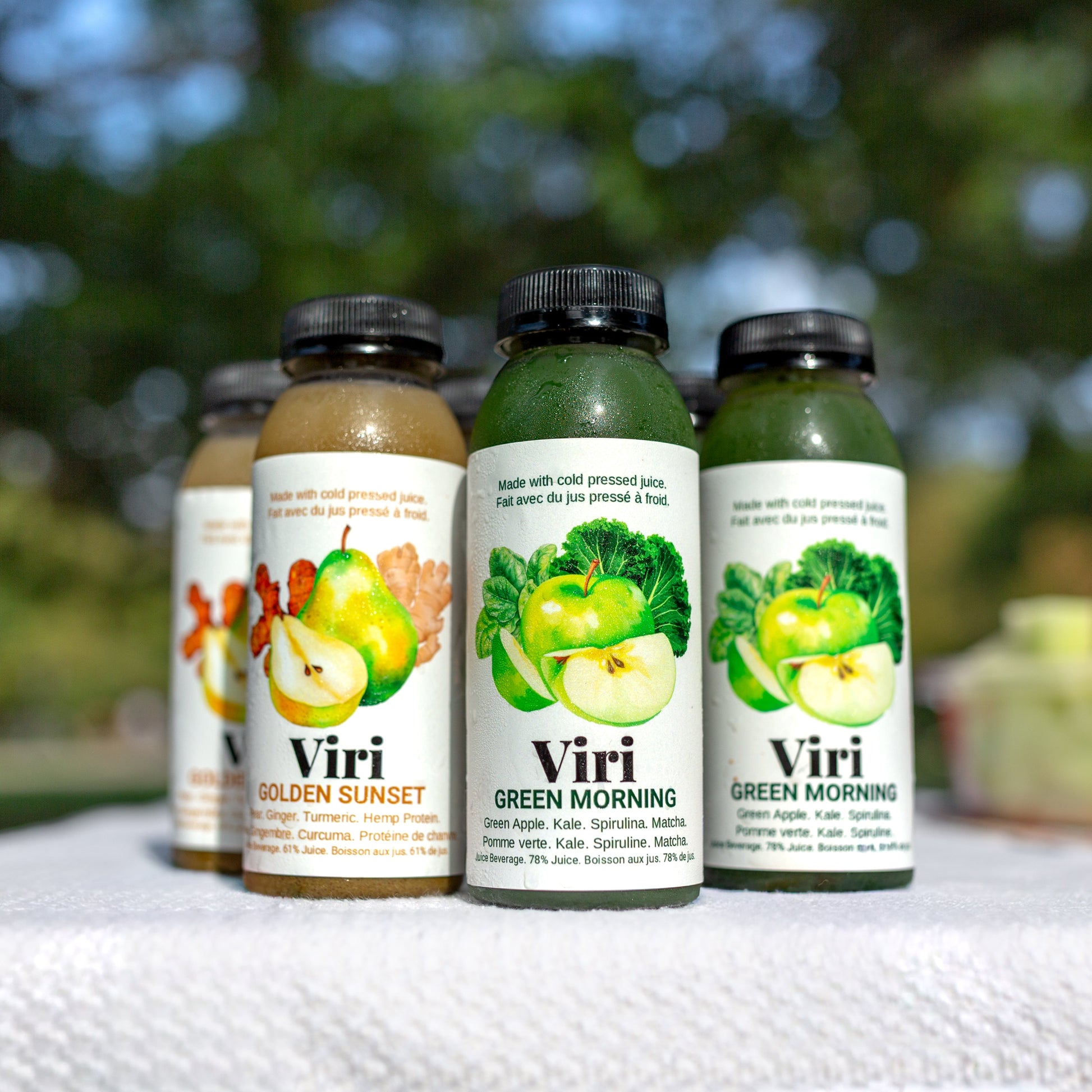Four bottles of Viri juice beverages with colourful labels on a white surface outdoors.